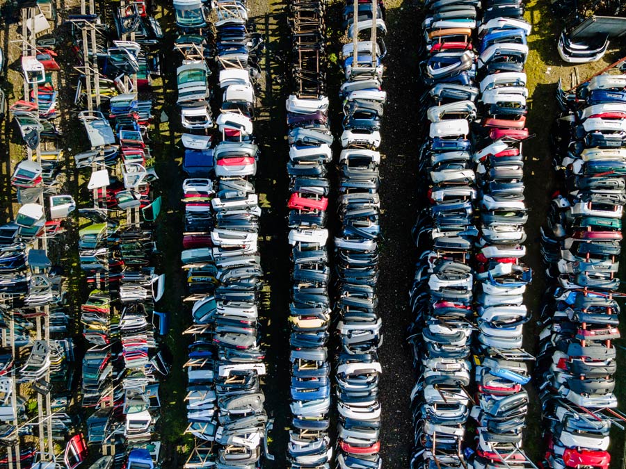 Une vue aérienne d'un centre de recyclage automobile où des parechocs de voitures démontés sont stockés en racks.