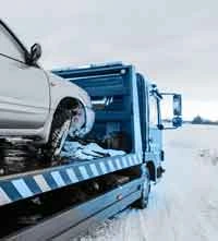 Une épave de voiture entrain d'être enlevée par une dépanneuse dans un terrain neigeux.